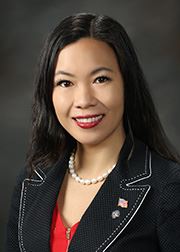 Portrait photo of Elizabeth Yang in a black suite with a cityscape background.